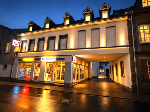 Abendliche Straßenszene mit Reisebüro.png - Frei ab sofort 2-Zimmer-Wohnung im 1. Obergeschoss Einbauküche Ohne Balkon Ohne PKW-Stellplatz