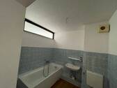 Badezimmer mit blauen Wandfliesen, sowie einem Deisgn-Vinylboden in Holzoptik, sowie einer weißen Badewanne, Waschtisch und einem Stand WC. - 