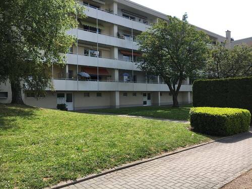 Eingangsbereich des mehrstöckigen Wohngebäudes umgeben von Grünanlagen mit Bäumen und Sträuchern - Nachmieter für Wohnung mit Fernblick gesucht!