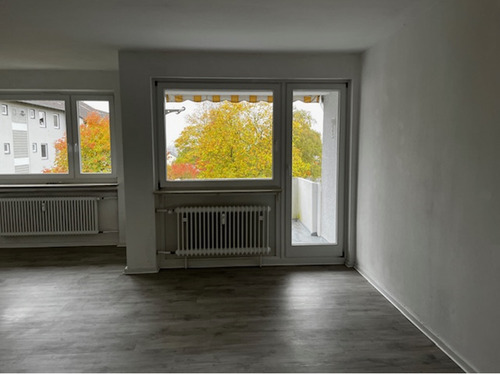 Wohn- und Essbereich mit Blick zu Fensterfront und Zugang zum Balkon, heller Bodenbelag und helle Wände.PNG - 3 Zimmer Etagenwohnung zur Miete in Baunatal