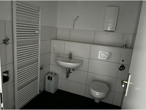 modernes Badezimmer mit Handtuchheizkörper, wandhängendem WC, großformatigen Fliesen in weiß (Wand) und dunkelgrau (Boden).PNG - 