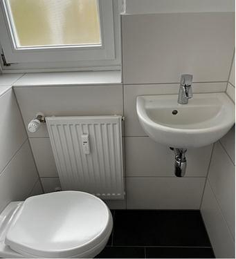 Gäste WC mit wandhängender Toilette, hellen Wand- und dunklen Bodenfliesen.PNG - 