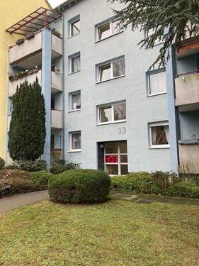 Eingangsbereich des mehrstöckigen Wohngebäudes umgeben von Grünanlagen mit Bäumen - Nachmieter für 3-Zimmerwohnung in ruhiger Lage gesucht!