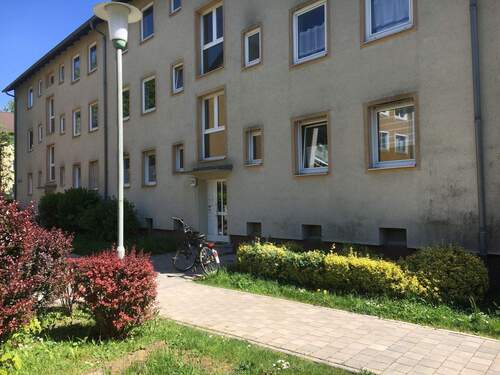 Vorderansicht eines mehrstöckigen Wohngebäudes umgeben von Hecken und grünen Sträuchern. - KLEIN, FEIN, MEIN - Modernisierte 2-Zimmer-Wohnung sucht Nachmieter