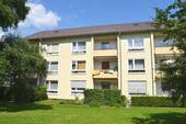 Rückansicht eines mehrstöckigen Wohngebäudes mit Balkonen, umgeben von Bäumen und grünen Sträuchern - Schicke 3-Zimmer-Wohnung - 682,00 EUR Kaltmiete, ca.  65,70 m² Wohnfläche