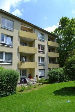 Rückansicht eines mehrstöckigen Wohngebäudes mit Balkonen, umgeben von Bäumen und grünen Sträuchern - 3 Zimmer Etagenwohnung zur Miete in Kassel