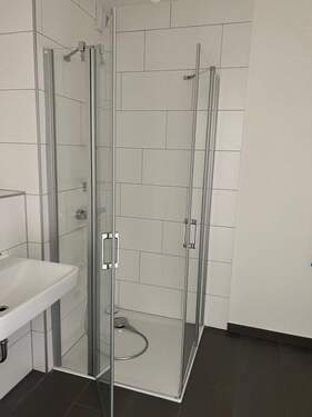 Beispiel eines Badezimmers mit Dusche, weißem Wandwaschbecken und Glas-Duschabtrennung mit weißen Wandfliesen auf anthrazitfarbenen Fliesenboden - 