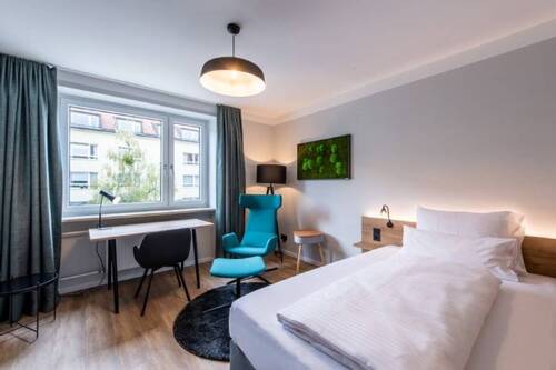 Schlafzimmer 2 mit Bett, Arbeitsbereich und Sitzecke sowie Flatscreen-TV - 2 Zimmer Etagenwohnung zur Miete in München