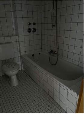 Badezimmer mit Blick auf Wanne und WC, deckenhohe weiße Wandverfliesung und helle Bodenfliesen.JPG - 