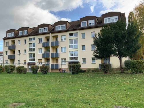 Gebäude Vorderseite des mehrstöckigen Wohnhauses umgeben von Grünanlagen mit Bäumen und Sträuchern - Kleine Familienwohnung sucht neue Mieter!