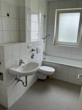 Bad mit Fenster, weißen Sanitärobjekten, weißen Wandfliesen und grauen Bodenfliesen - Etagenwohnung mit 70,90 m&sup2; in Bad Vilbel zur Miete