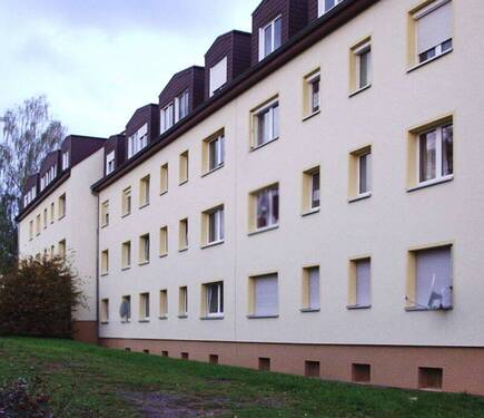 Rückansicht des mehrstöckigen Wohngebäudes umgeben von Grünanlagen mit Bäumen und Sträuchern - 