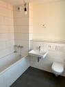 Beispiel eines Badezimmers mit weißem Wand-WC, weißem Wandwaschbecken und Badewanne mit weißen Wandfliesen auf anthrazitfarbenen Fliesenboden - 
