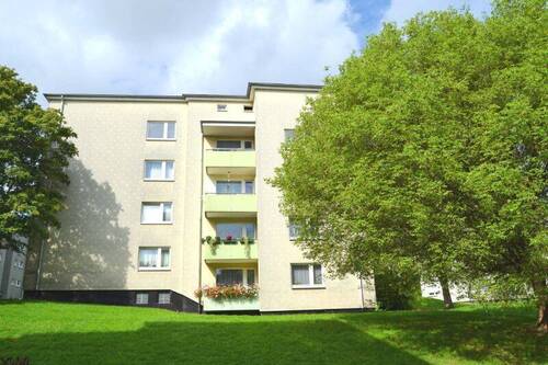  Rückansicht eines mehrstöckigen Wohngebäudes mit Balkonen, umgeben von Bäumen und grünen Sträuchern - Schicke 3-Zimmer-Wohnung mit neuem Bad