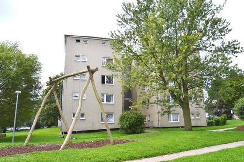  Rückansicht eines mehrstöckigen Wohngebäudes mit Balkonen, umgeben von Bäumen und grünen Sträuchern - 3 Zimmer Etagenwohnung zur Miete in Kassel
