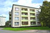  Rückansicht eines mehrstöckigen Wohngebäudes mit Balkonen, umgeben von Bäumen und grünen Sträuchern - 3 Zimmer Etagenwohnung in Kassel