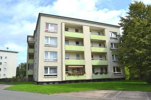  Rückansicht eines mehrstöckigen Wohngebäudes mit Balkonen, umgeben von Bäumen und grünen Sträuchern - 3 Zimmer Etagenwohnung in Kassel
