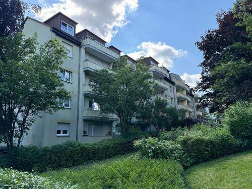 Rückansicht des mehrstöckigen Wohngebäudes mit Balkonen, umgeben von Grünanlagen mit Bäumen und grünen Sträuchern - 