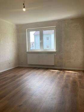 Wohnzimmer mit neuem Fußbodenbelag in Holzoptik, Wände sind tapezierfertig vorbereitet - 