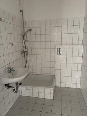 Bad mit Dusche, weißen Sanitärobjekten, Waschmaschinenanschluss, weiß-grauen Wandfliesen und weißen Bodenfliesen - 