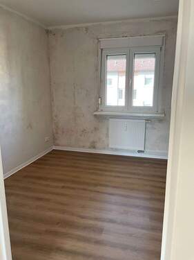 Schalfzimmer mit Fenster, braunem Boden und weißer Decke. Wände sind tapezierfähig vorbereitet..JPG - 