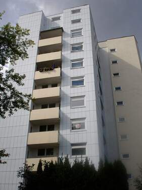 Rückansicht eines mehrstöckigen Wohngebäudes mit Balkonen, umgeben von Bäumen und grünen Sträuchern - 3 Zimmer Etagenwohnung zur Miete in Kassel