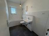 Blick in Bad mit weißen Wandfliesen, weißem Waschbecken, grauen Bodenfliesen, Hänge-WC und Badewanne mit Duschvorrichtung und Fenster - 3 Zimmer Etagenwohnung zur Miete in Meerbusch