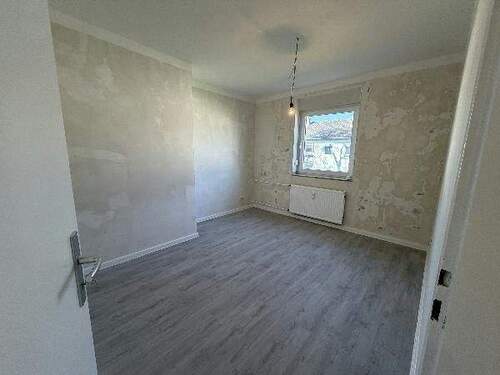 Blick in Schlafzimmer mit grauem PVC-Boden und tapezierfähigen Wänden mit einem weißen Fenstern - 