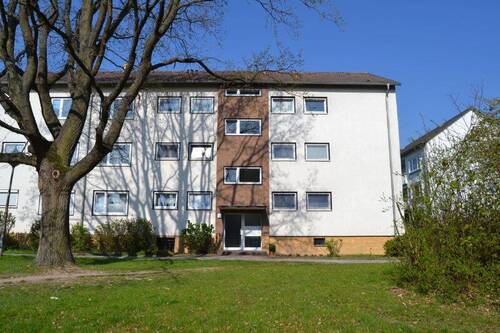 Akazienallee 62: Blick über die Grünanlage mit altem Baumbestand auf den barrierefreien Eingangsbereich eines mehrgeschossigen Wohngebäudes mit heller Fassade - 3 Zimmer Etagenwohnung zur Miete in Baunatal