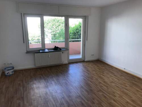 Wohnzimmer mit weißen Wänden, Bodenbelag in Holzoptik und Zugang zum Balkon - 3 Zimmer Etagenwohnung zur Miete in Bad Vilbel