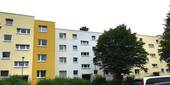 Eingangsbereich des mehrstöckigen Wohngebäudes umgeben von Grünanlagen mit Bäumen und Sträuchern - Nachmieter für kleine Familienwohnung gesucht!