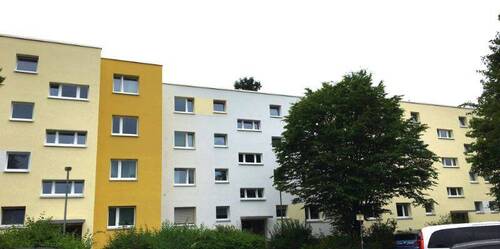Eingangsbereich des mehrstöckigen Wohngebäudes umgeben von Grünanlagen mit Bäumen und Sträuchern - Nachmieter für kleine Familienwohnung gesucht!