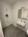 Badezimmer mit grauen Bodenfliesen und weißen Wandfliesen, bodengleicher Dusche und Waschbecken.JPG - 
