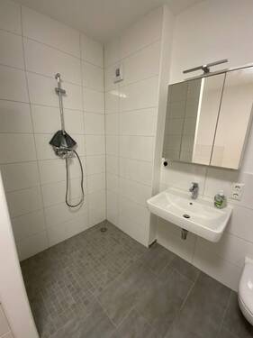 Badezimmer mit grauen Bodenfliesen und weißen Wandfliesen, bodengleicher Dusche und Waschbecken.JPG - 