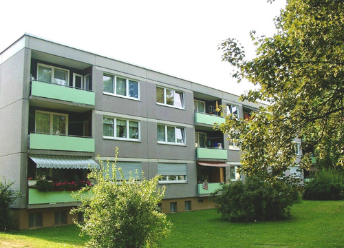 Rückansicht eines Mehrfamilienhauses mit Balkonen in grüner Umgebung Bäumen im Vordergrund - Großzügige 4-Zimmer-Wohnung im Erdgeschoss in Fritzlar