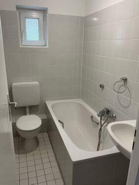 Badezimmer mit hellen, türhohen Fliesen, einer Badewanne und einer Toilette - 