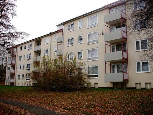 Rückansicht eines mehrstöckigen Wohngebäudes mit Balkonen, umgeben von Bäumen und grünen Sträuchern - Schicke 3-Zimmer-Wohnung - 653,00 EUR Kaltmiete, ca.  72,50 m² Wohnfläche