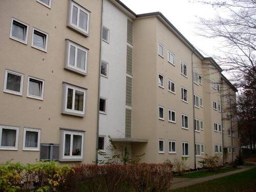 Vorderansicht eines mehrstöckigen Wohngebäudes mit Balkonen, umgeben von Bäumen und grünen Sträuchern - 3 Zimmer Etagenwohnung zur Miete in Kassel