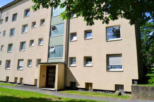 Vorderansicht eines mehrstöckigen Wohngebäudes , umgeben von Bäumen und grünen Sträuchern - Schicke 3-Zimmer-Wohnung - 485,00 EUR Kaltmiete, ca.  63,60 m² Wohnfläche