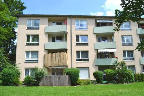 Rückansicht eines mehrstöckigen Wohngebäudes mit Balkonen, umgeben von Bäumen und grünen Sträuchern - 3 Zimmer Etagenwohnung in Kassel
