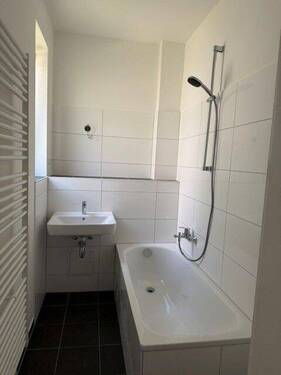 Tageslichtbad mit Badewanne, weißem Waschbecken, weißen Wandfliesen, dunkelgrauen Bodenfliesen und Handtuchkeizkörper - 