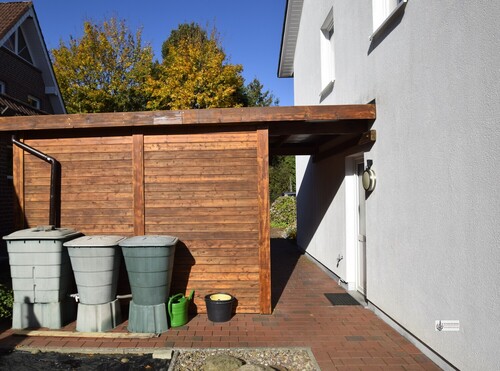 Holzhaus frisch gestrichen mit Regenwassertonnen und Türüberdachung - 